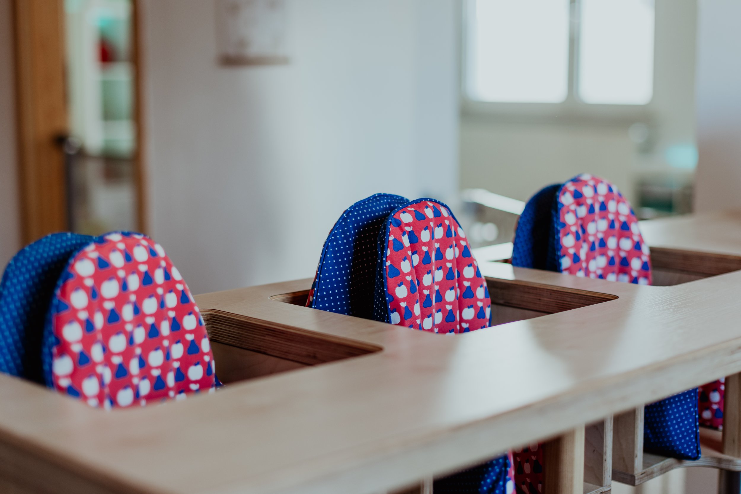 Bunte Schulrucksäcke hängen in einem Klassenraum auf einer Holzablage.