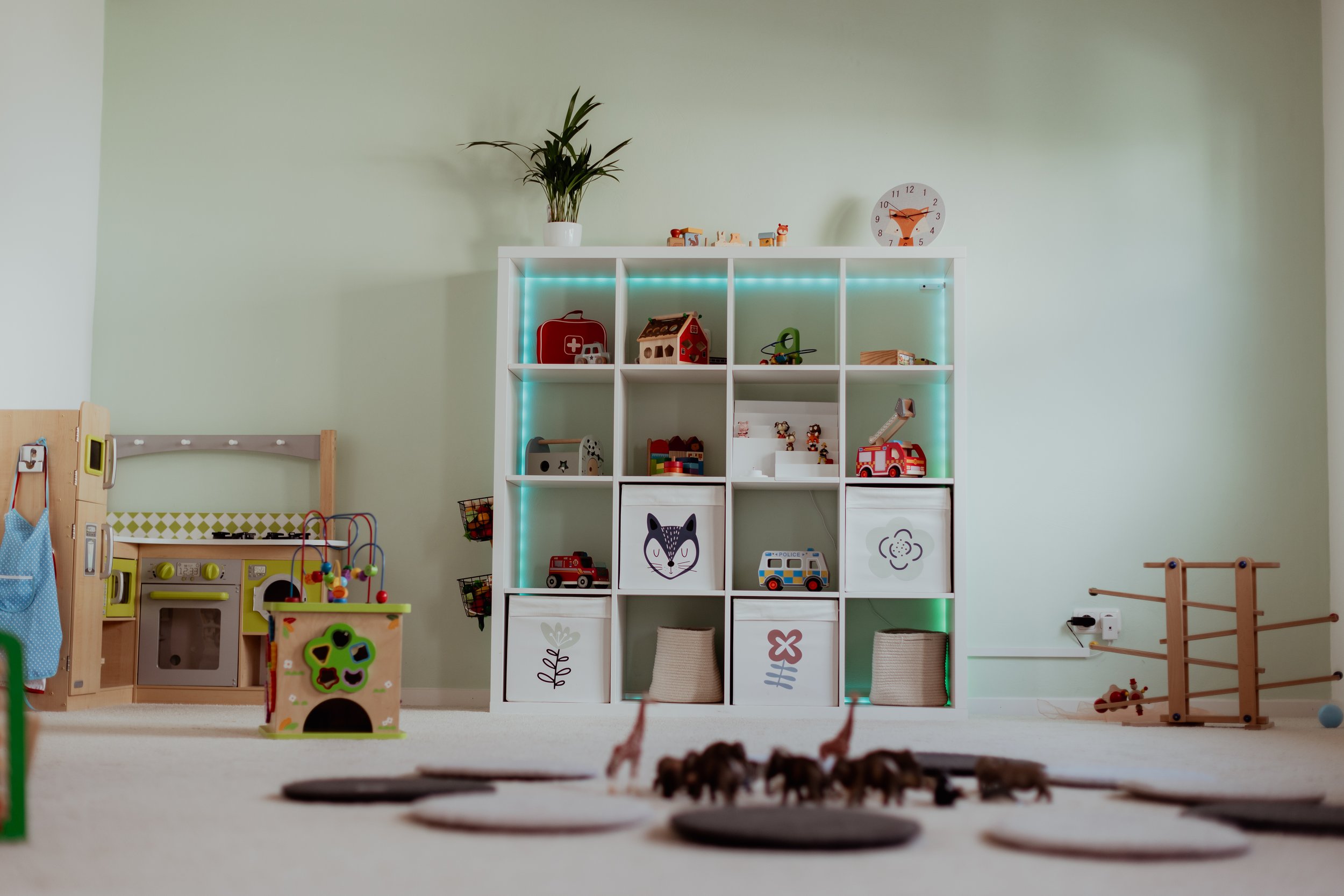 Kinderzimmer mit Spielzeug und Regalen, grüne Wand, heller Teppichboden, uhr
