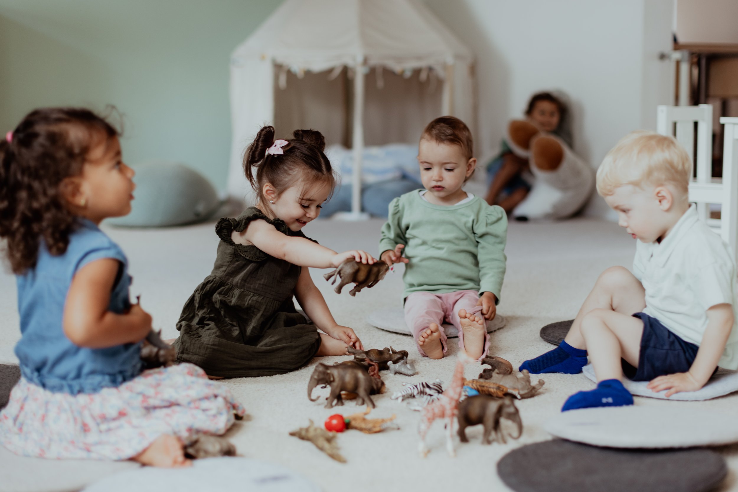 Vier Kinder sitzen im Kreis auf dem Boden und spielen mit Spielzeugtieren.