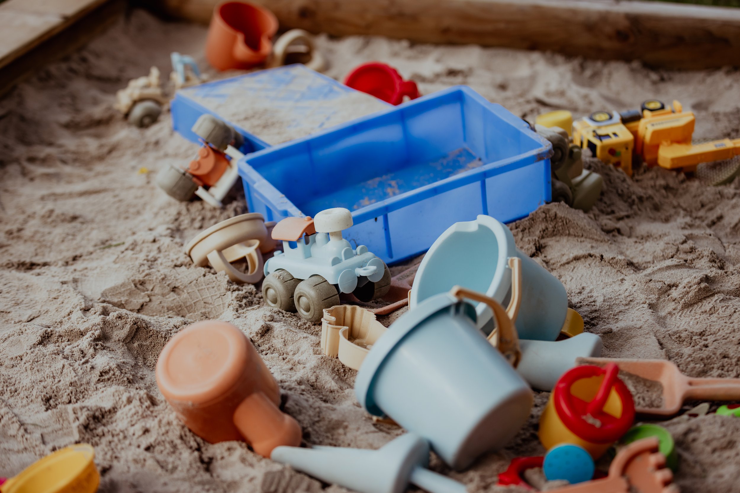 Sandkasten mit buntem Sandspielzeug wie Eimer, Schaufeln, Bagger, und Tieren